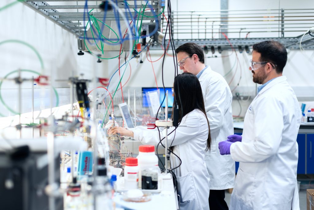 man in white lab suit standing in front of white and red plastic bottles